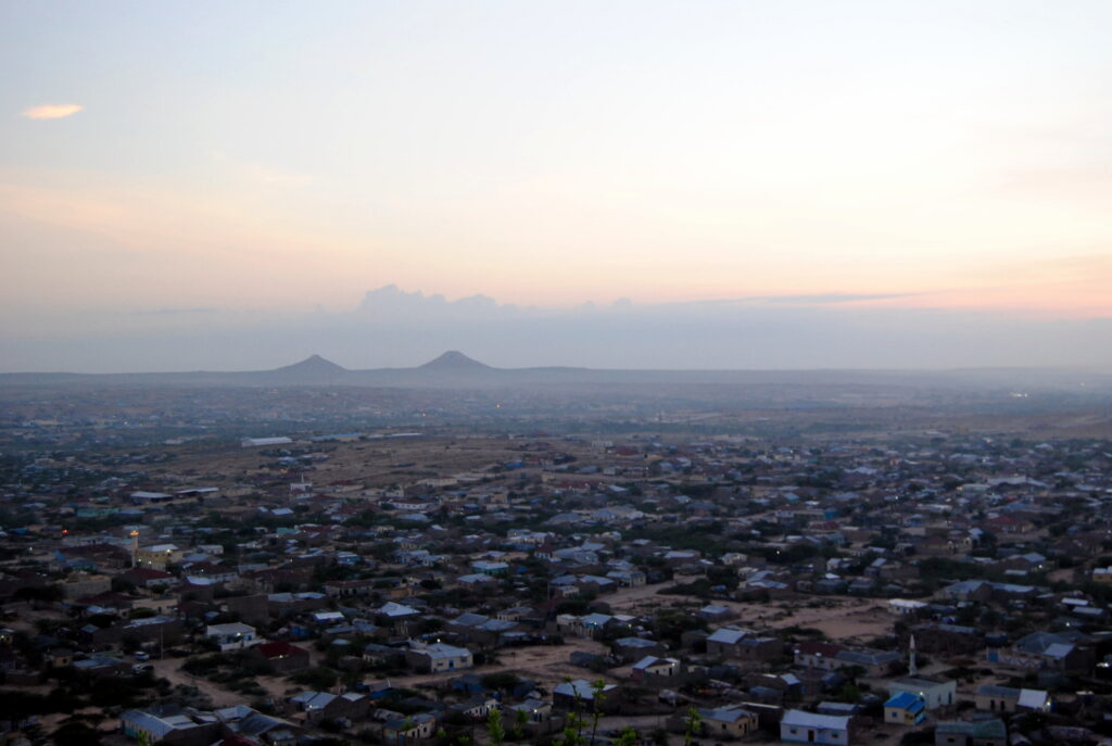a skyline of a city at dawn, with two mountains visible in the distance