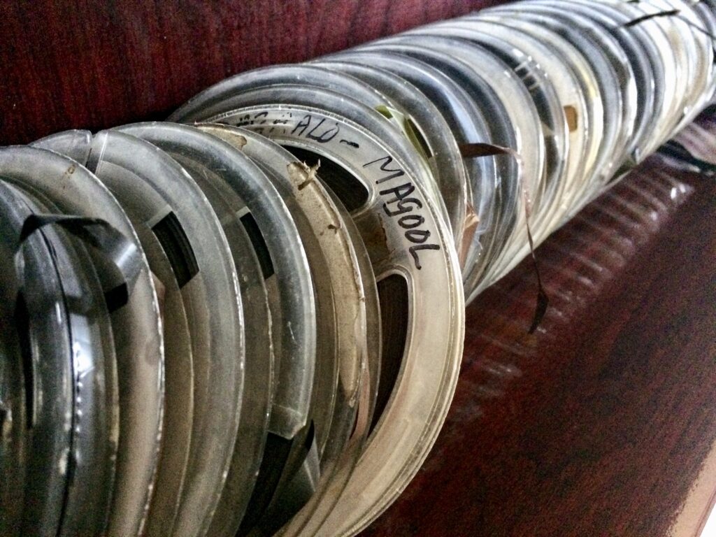 reel-to-reel cassettes lined up on a shelf, featuring one labelled 'Magool'