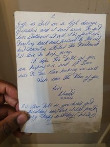 May's hand holding up the second page of a handwritten letter, swapping family news and birthday wishes and signed off "Love, Eleanor xxxx"