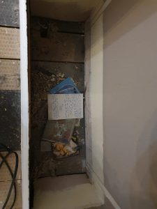Letter, postcards and a baby photo lying in a hole in the floor where a built-in bookcase used to be, in among some building debris, photographed from above.